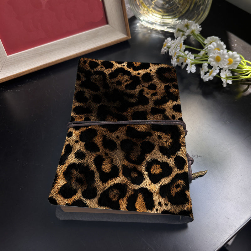 Leopard print notebook on a dark surface with a glass and flowers in the background